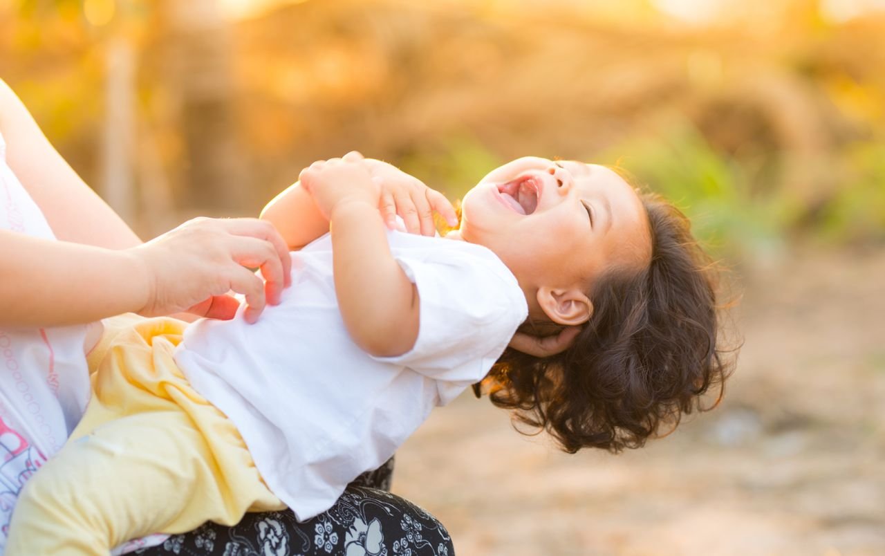 who-we-are A happy baby enjoying playful moments outdoors, captured in warm summer lighting.