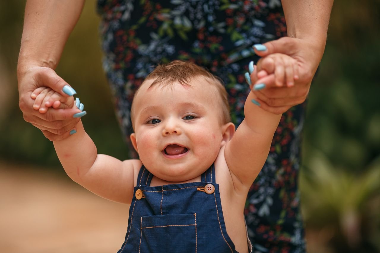 services-04 Cute baby in denim overalls held by adult hands, smiling outdoors.