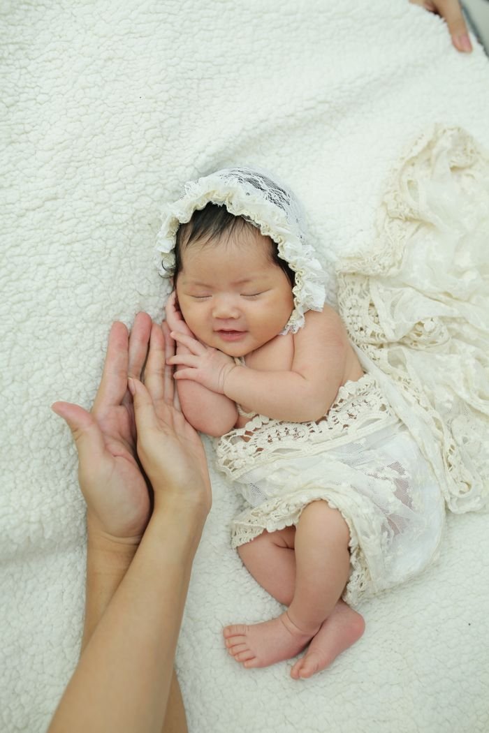 about-bg Charming newborn baby in lace bonnet and wrap sleeping peacefully, supported gently by adult hands.