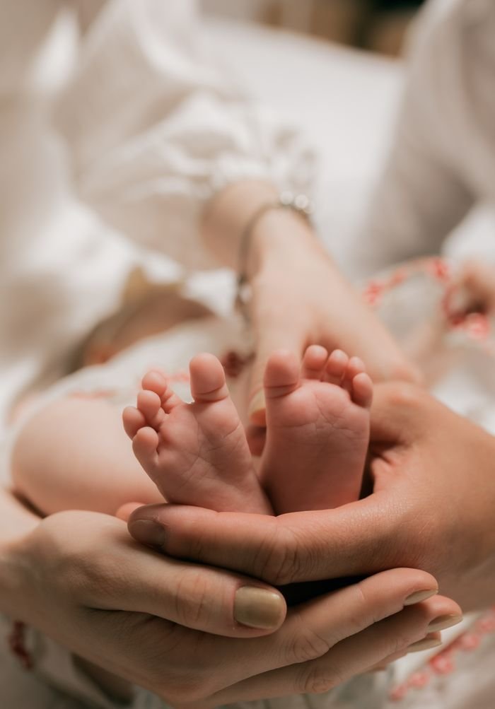 services-03 A close-up of a baby's tiny feet cradled gently by loving parents' hands in a warm setting.