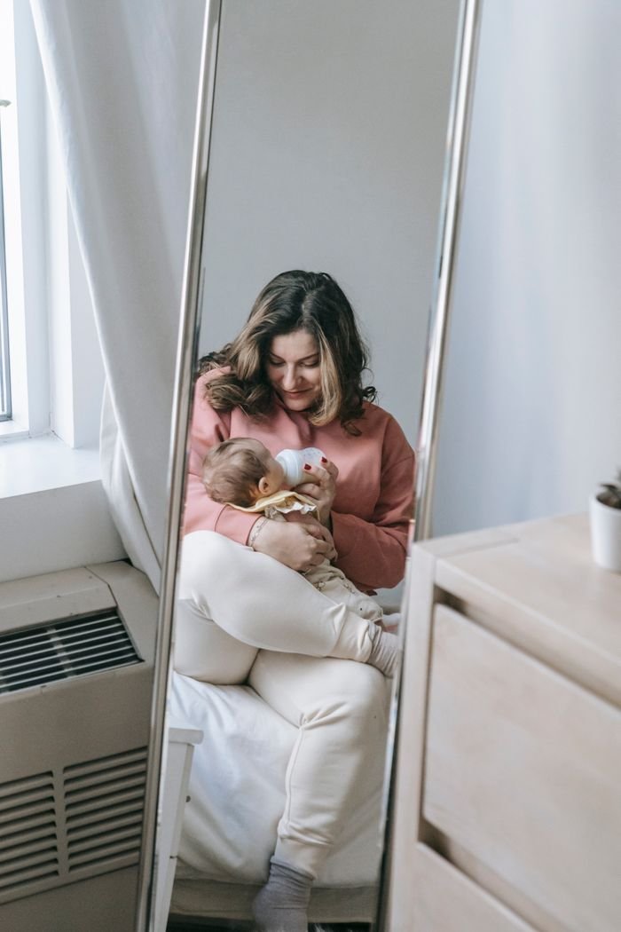 Crafting Captivating Headlines: Your awesome post title goes here A tender moment of a mother bottle-feeding her baby indoors through a mirror reflection.